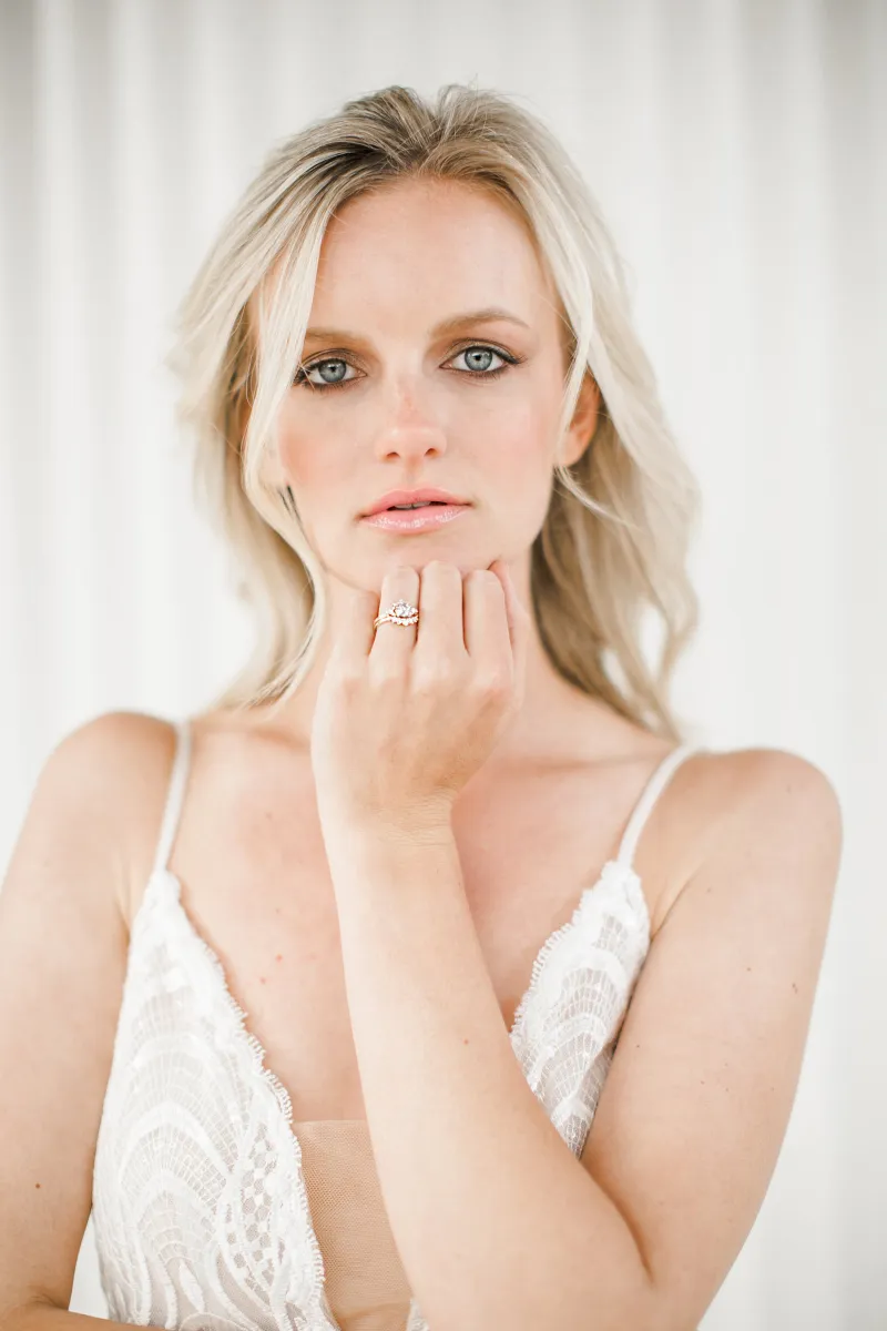 A bride resting her chin on her hand with her engagement ring in frame.
